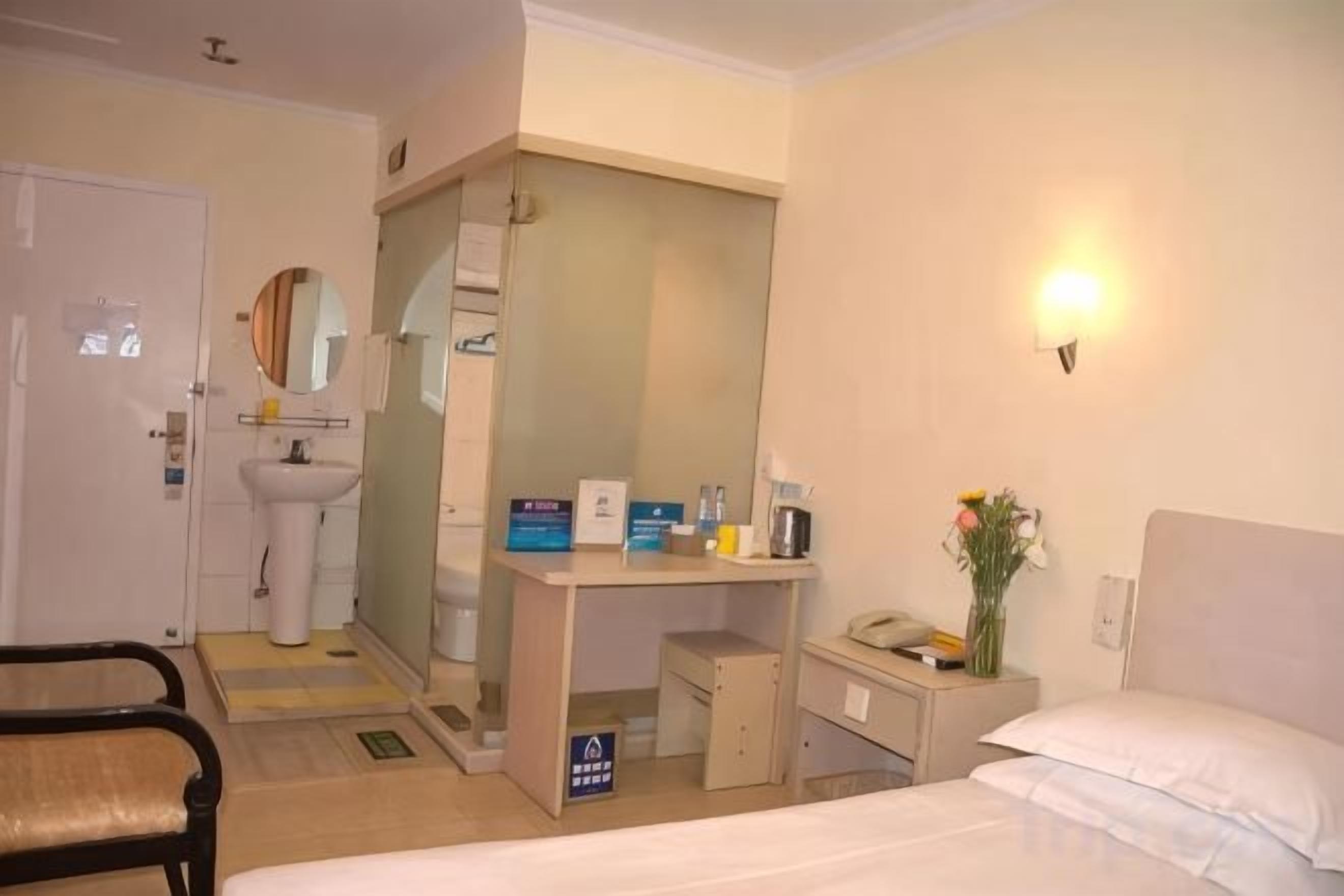 A hotel room with a bed, a desk with a chair, a sink, and a mirror.