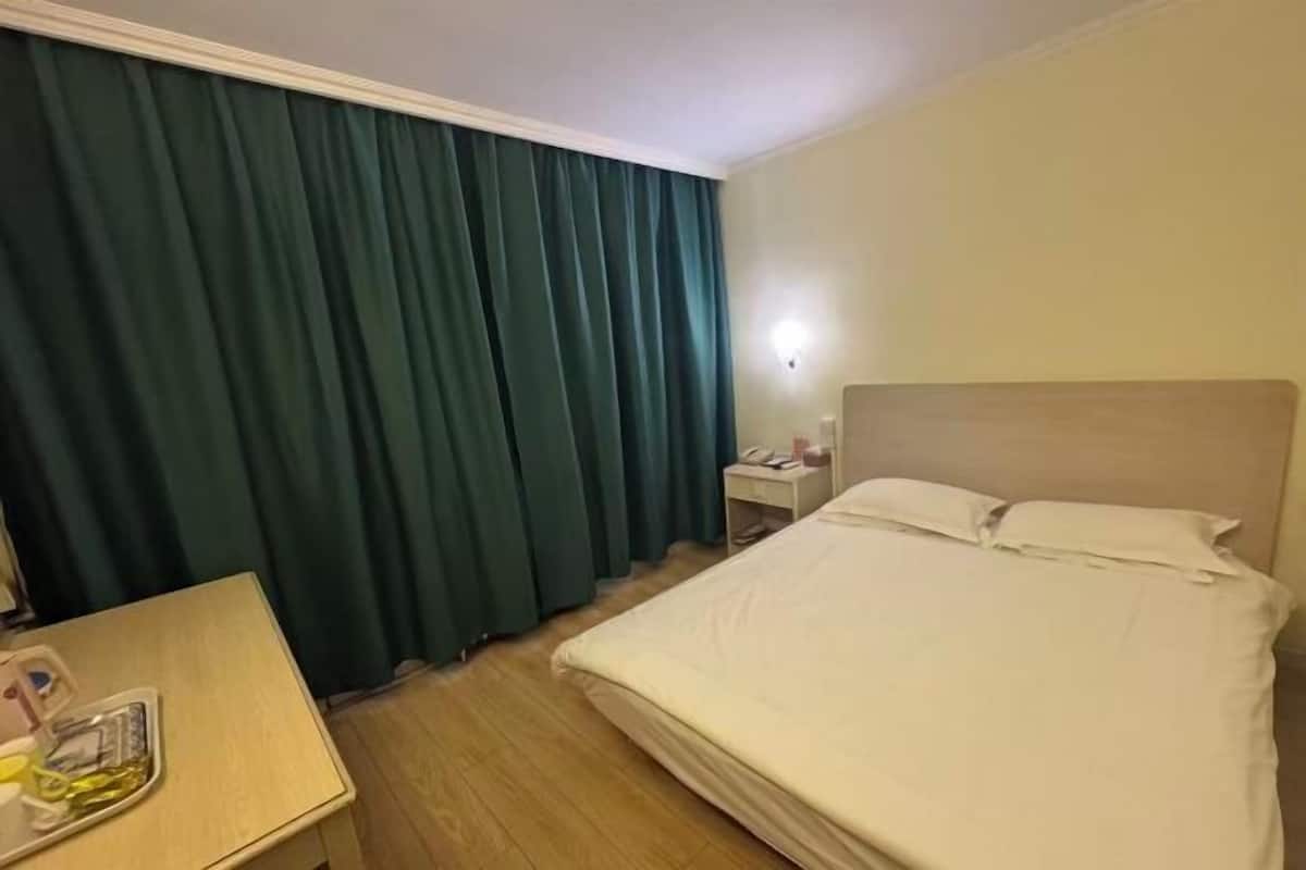 A hotel room with a bed, a desk, a nightstand, and a window with curtains.