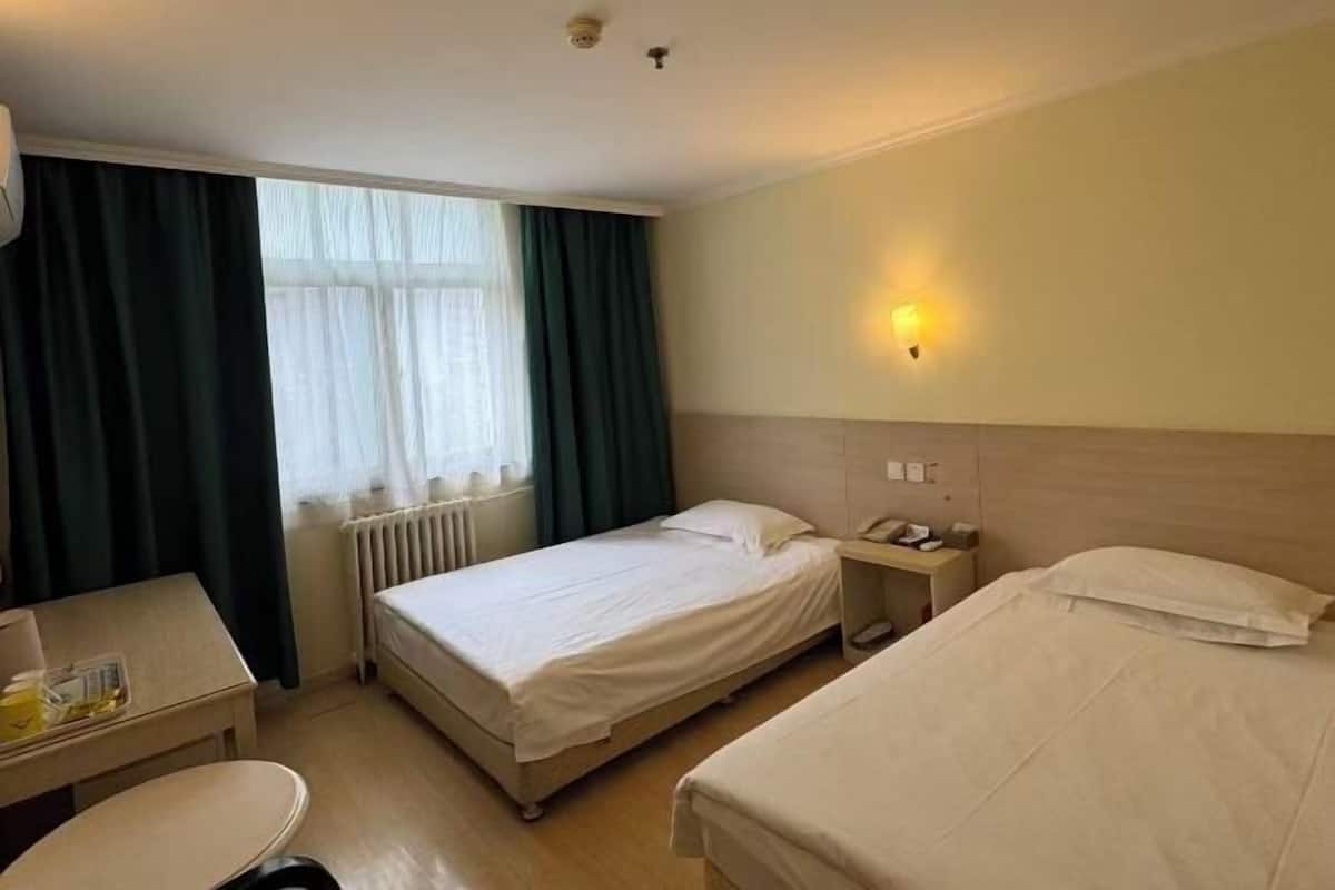 A hotel room with two beds, a desk, a chair, and a window with curtains.