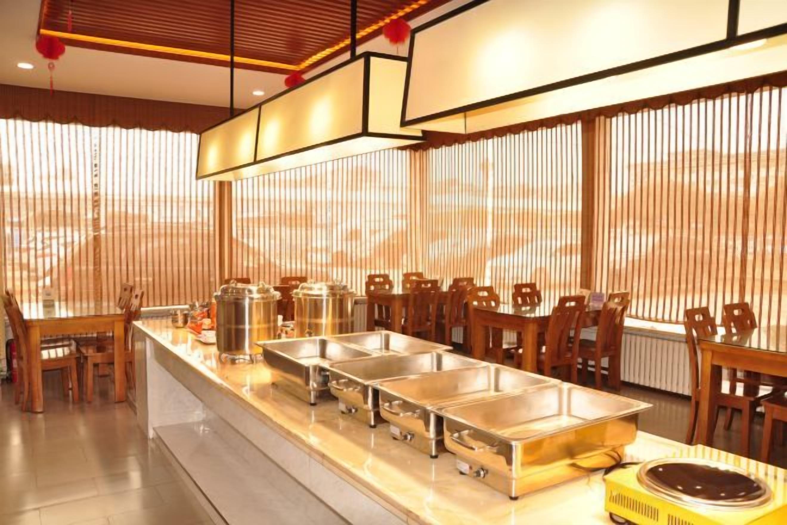 A buffet setup with multiple serving stations, a dining area with chairs, and a window with vertical blinds.