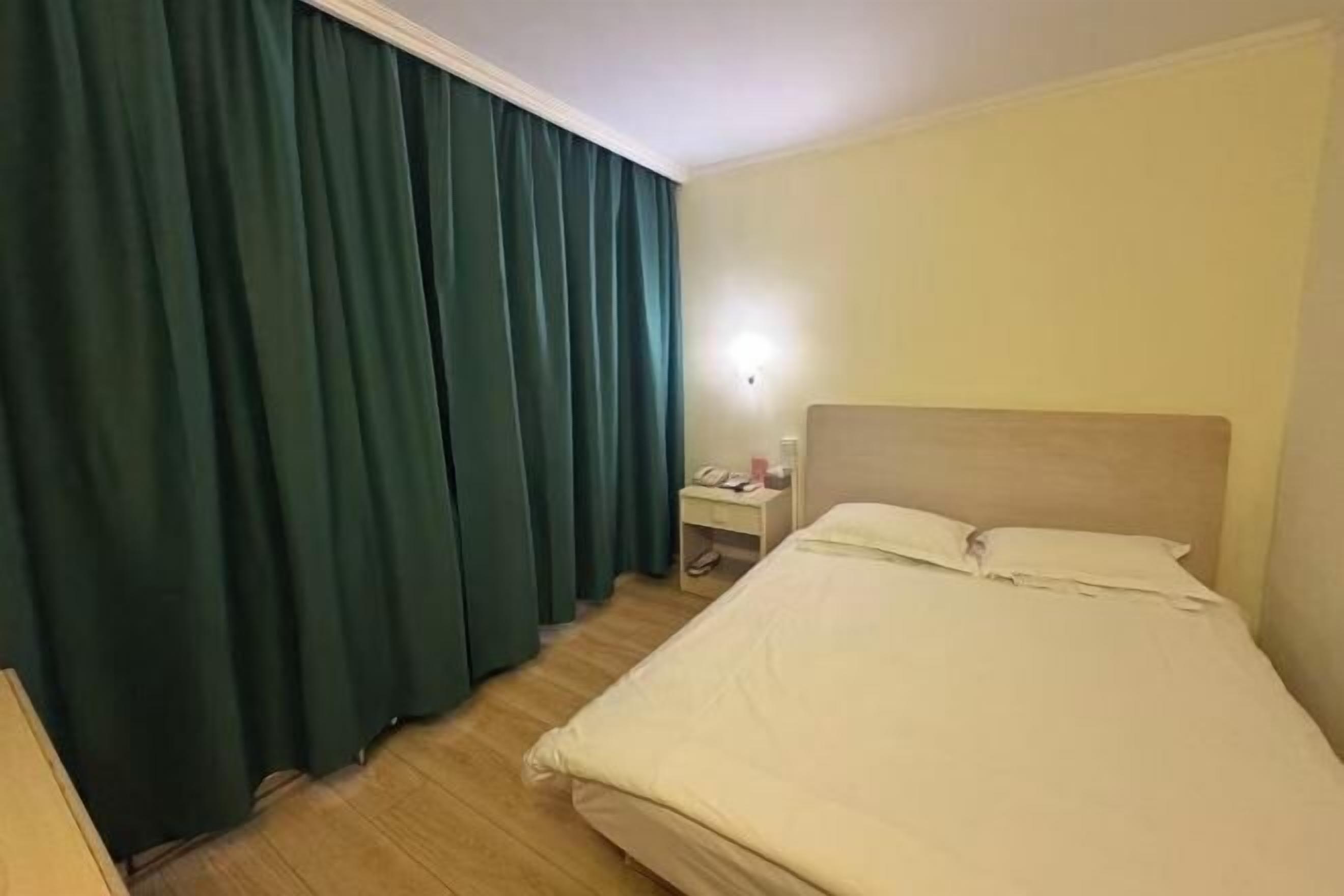 A hotel room with a bed, a nightstand, a lamp, and a window with curtains.