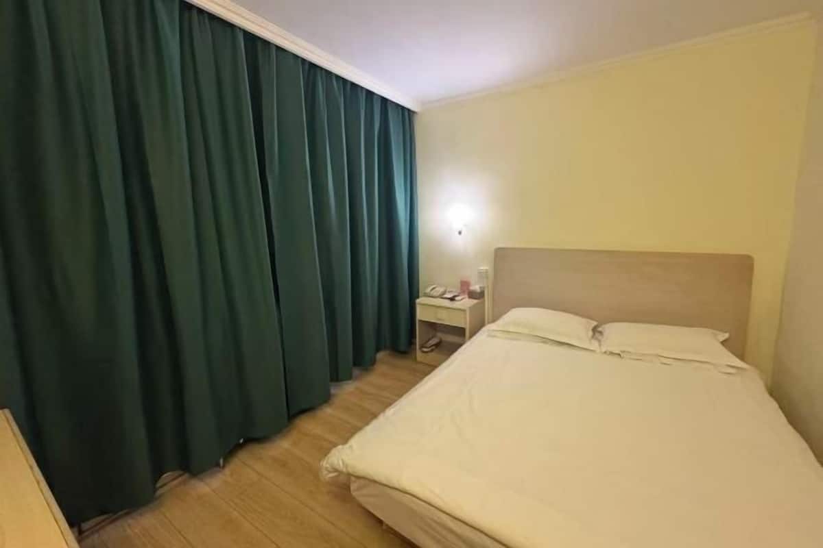 A hotel room with a bed, a nightstand, a lamp, and a window with curtains.