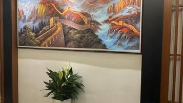 Un cuadro enmarco de la Gran Muralla China sobre una pared, una planta en maceta y una puerta de madera con listones verticales.