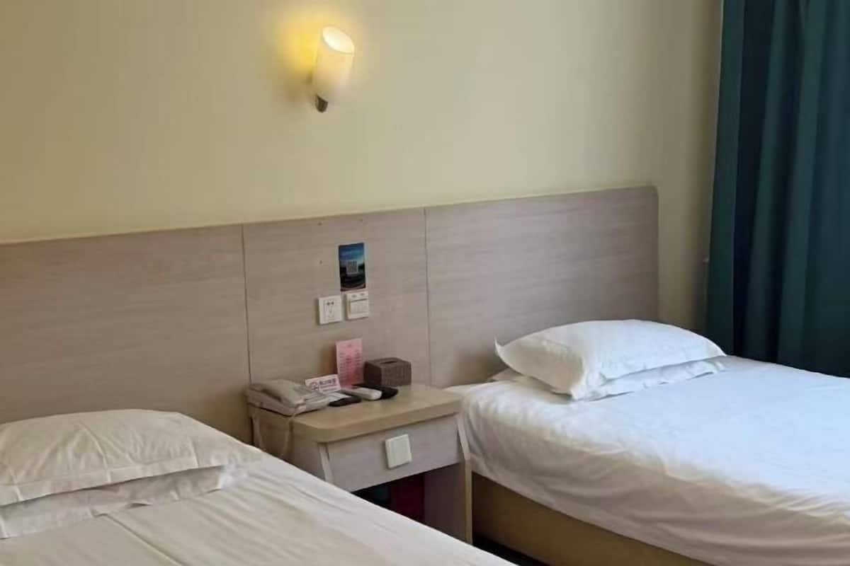 A hotel room with two beds, a nightstand with a lamp, a phone, and a small table with a box.