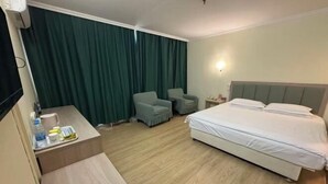 A hotel room with a bed, a desk, two chairs, a TV, and a curtain.