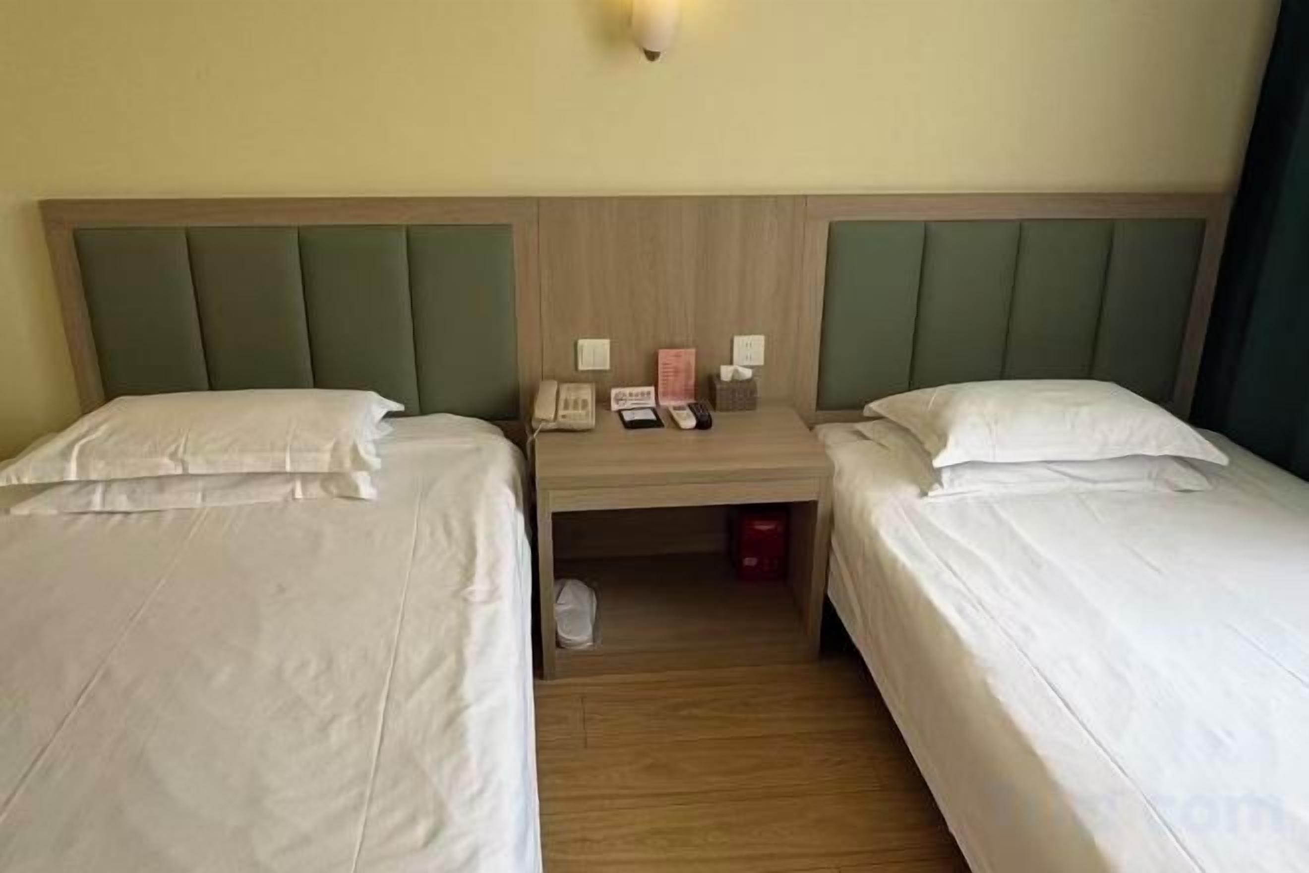 A hotel room with two single beds, a nightstand with a telephone and a trash bin, and a light fixture above the headboard.