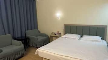 A hotel room with a bed, two chairs, a nightstand, and a lamp.