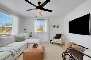 A modern living room with a sectional sofa, a coffee table, a chair, a television, and a ceiling fan. - Spacious & Updated 4-bedroom home w/BBQ, fire pit & AC in the Heart of Missoula! (Missoula)
