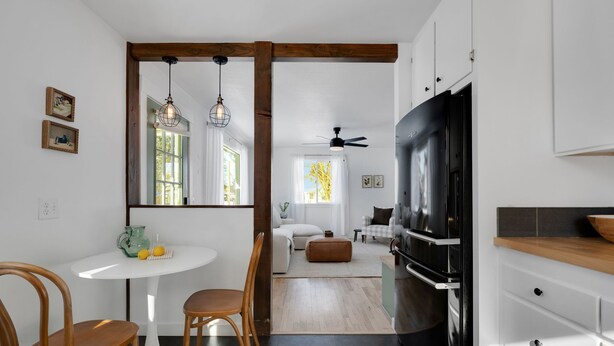 A modern kitchen with a black refrigerator, wooden cabinets, and a dining area with a white table and wooden chairs. - Spacious & Updated 4-bedroom home w/BBQ, fire pit & AC in the Heart of Missoula! (Missoula)