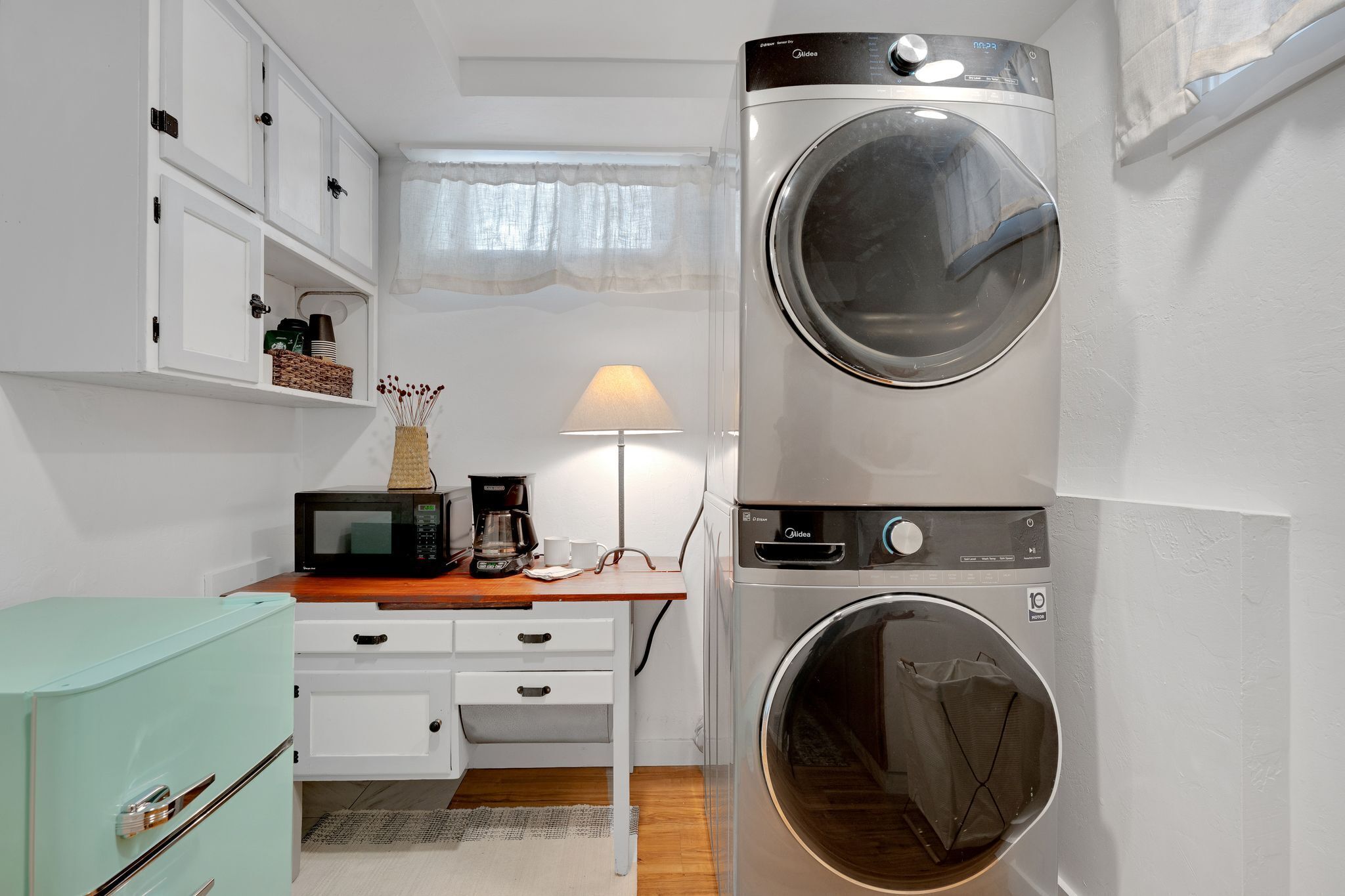A compact laundry room with a washing machine and dryer stacked vertically, a microwave, a coffee maker, and a small refrigerator.
