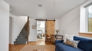 A modern living room with a staircase, a blue sofa, a coffee table, and a wooden door. - Spacious & Updated 4-bedroom home w/BBQ, fire pit & AC in the Heart of Missoula! (Missoula)
