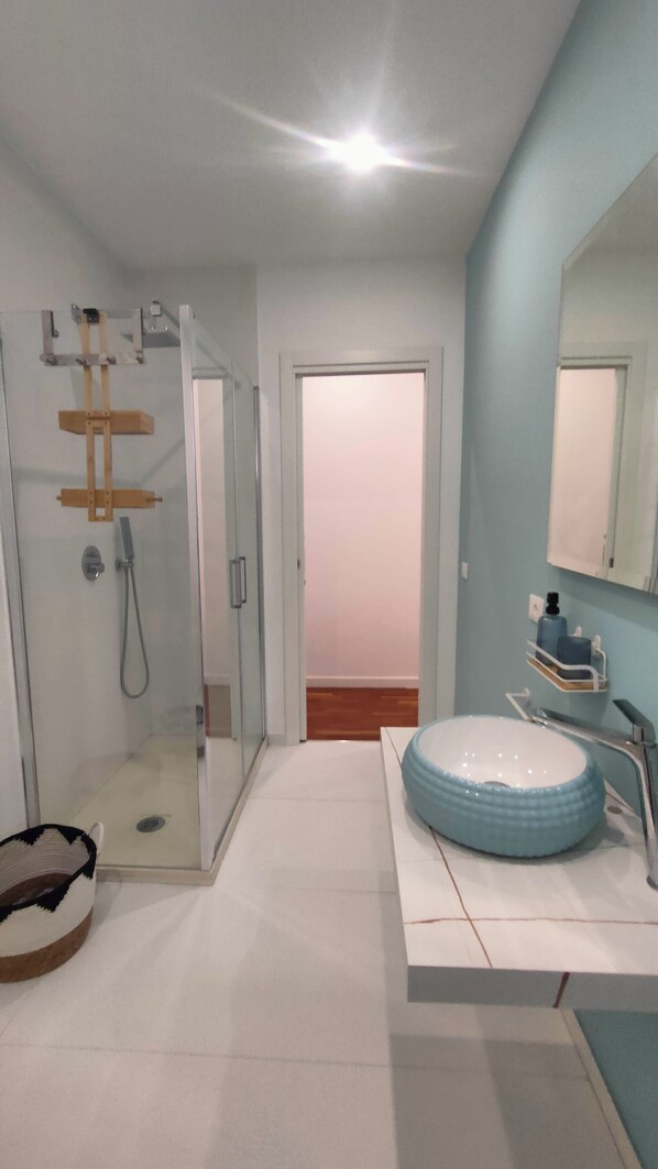 A modern bathroom with a glass shower enclosure, a large sink with a blue basin, and a mirror above the sink.