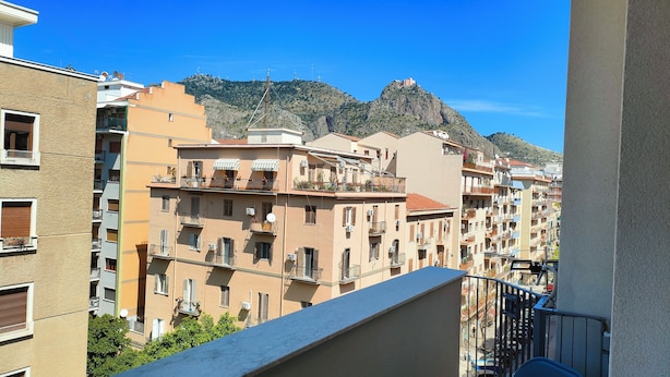 A multi-story residential building with balconies, a mountain in the background, and a clear sky. - Elegant Apartment with Terrace – A Peaceful Oasis in Palermo (Palermo)