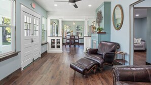A spacious room with a wooden floor, a ceiling fan, a dining area with a table and chairs, and leather furniture.