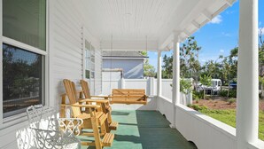 A covered porch with wooden furniture and a white railing.
