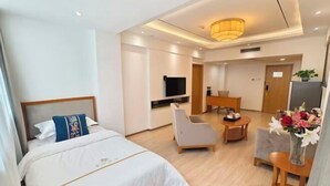 A hotel room with a bed, a desk, a chair, a TV, and a vase of flowers. - Xuesong Hostel (Beijing)