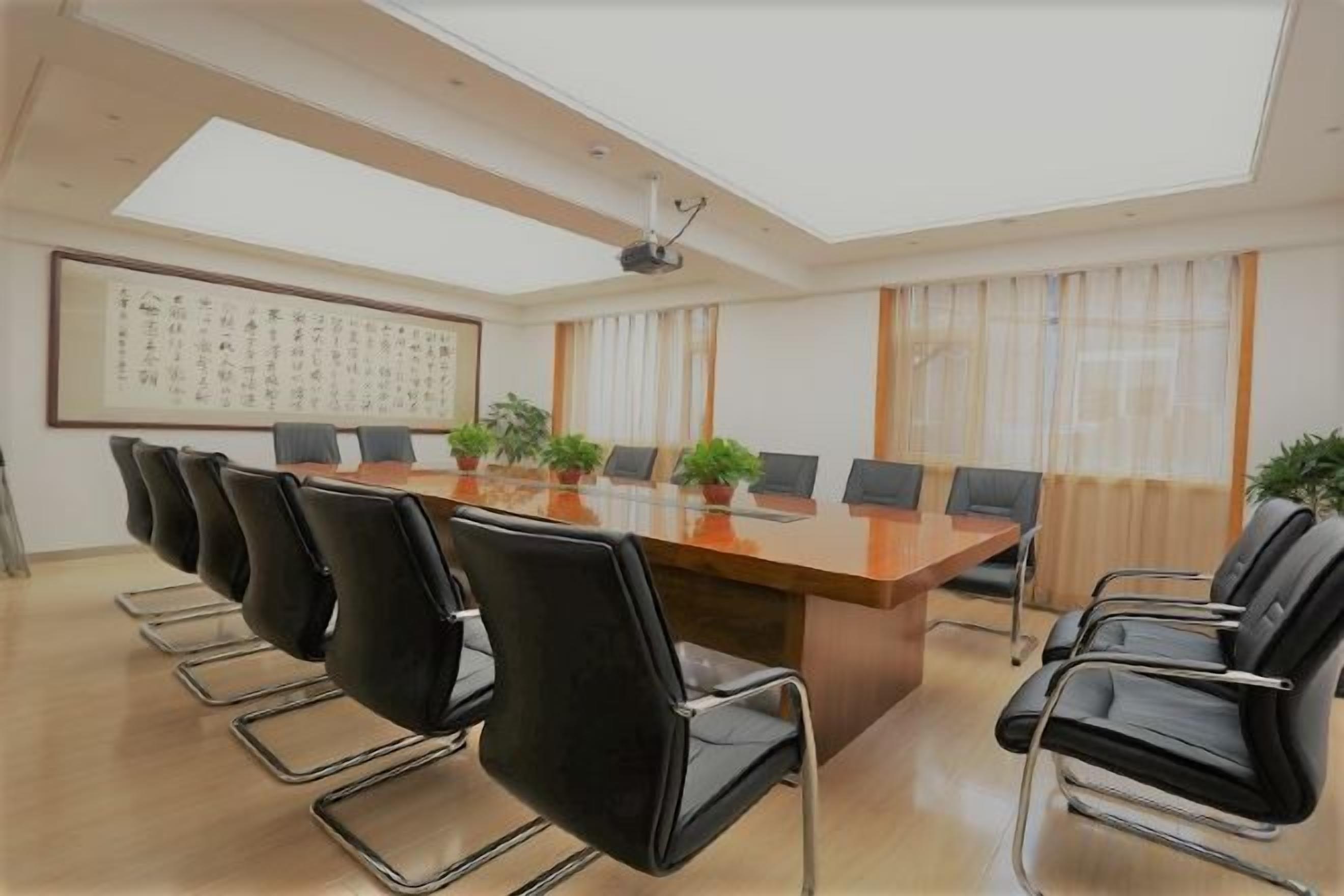 Une salle de conférence avec une longue table, des chaises noires et des plantes en pot.