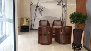 Een lobby met een groot wanddecor van bamboe, twee houten stoelen en een potplant.