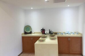 A kitchen with wooden cabinets, a countertop, and various kitchenware including a kettle, cups, and a teapot.
