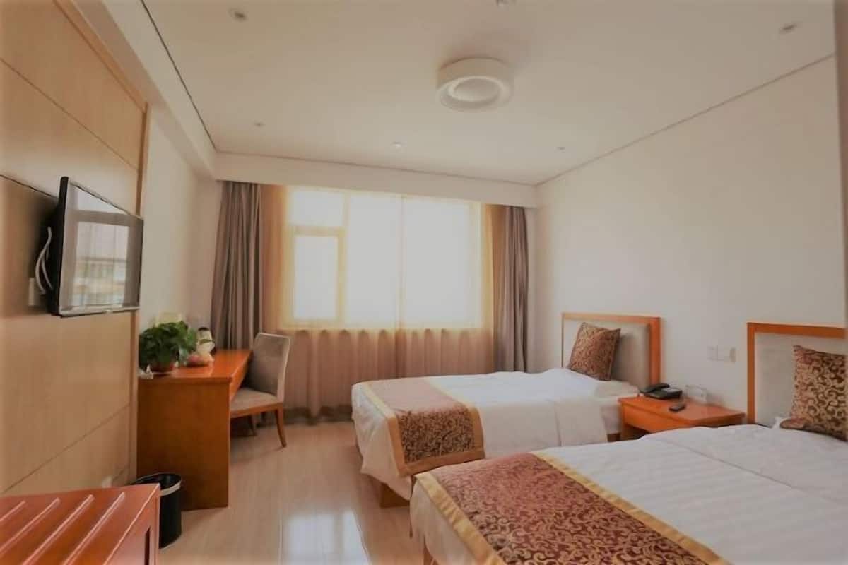 Camera d'albergo con due letti, una scrivania, una sedia, una televisione e una finestra con tende.