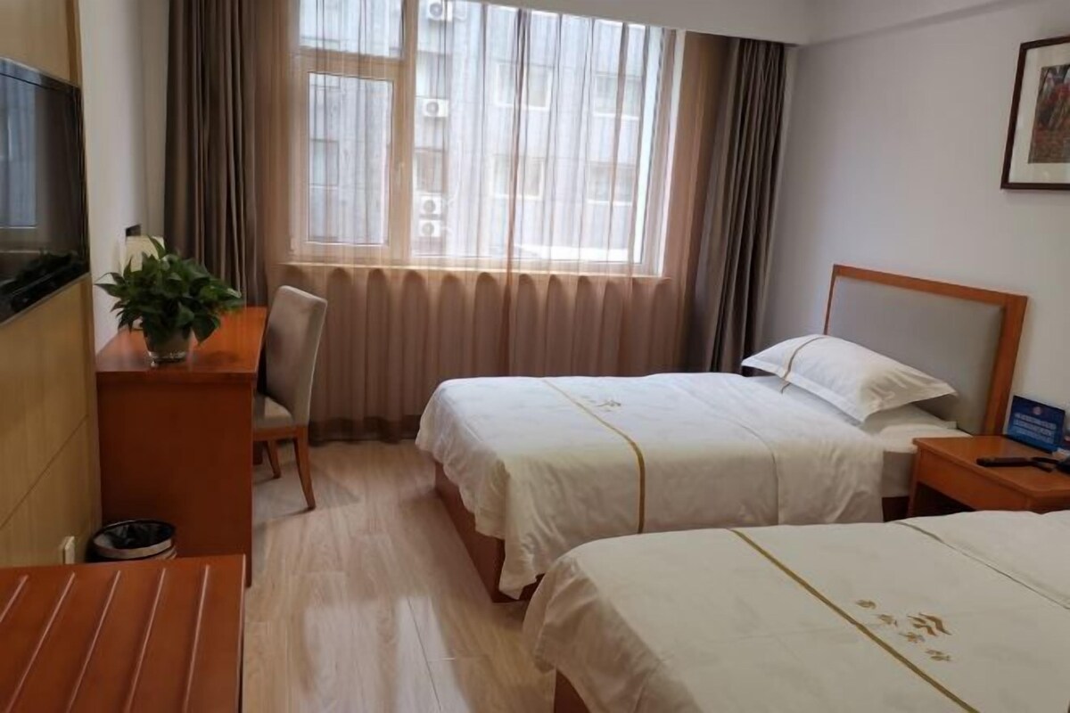 Une chambre d’hôtel avec deux lits, un bureau avec une chaise, une télévision et une fenêtre avec des rideaux.