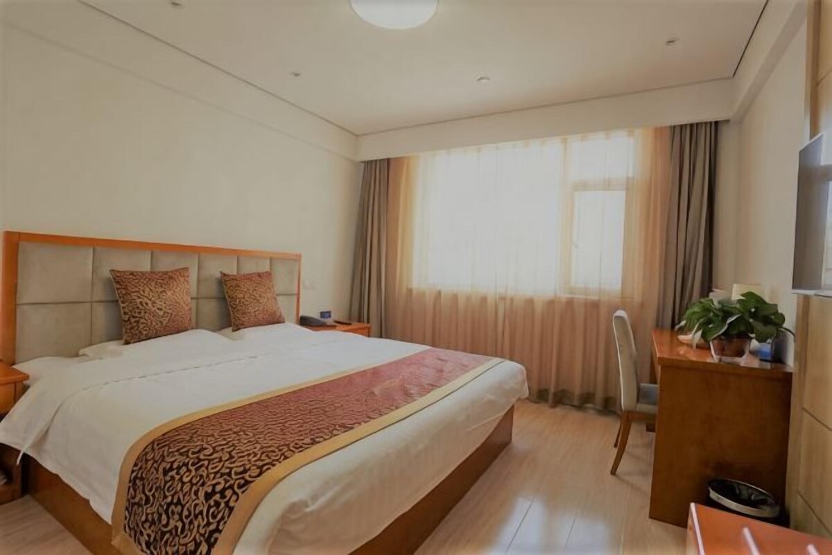 A hotel room with a large bed, bedside tables, a desk, and a TV.