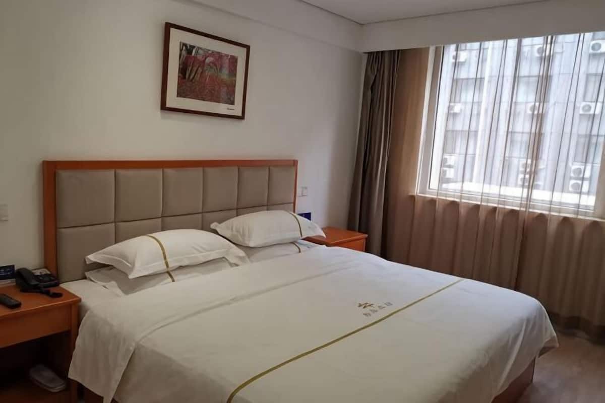 Una camera d'albergo con un letto grande, due comodini, un tavolino e una finestra con tende.
