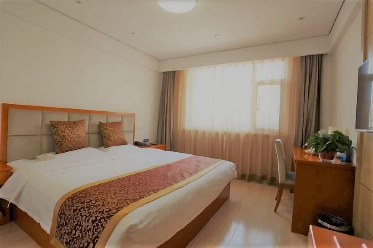 Una camera d'albergo con un letto grande, una scrivania con una sedia, una televisione e una finestra con tende.