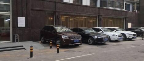 A row of parked cars in front of a building with a dark facade and multiple windows.