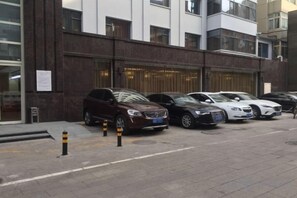 A row of parked cars in front of a building with a dark facade and multiple windows. - Xuesong Hostel (Beijing)