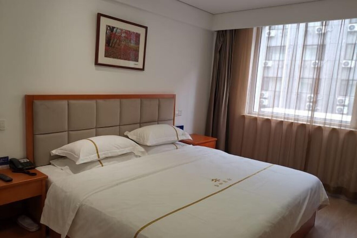 Une chambre d’hôtel avec un lit, une table de chevet avec un téléphone, un tableau encadré au mur et une fenêtre avec des rideaux.