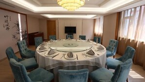 A conference room with a round table, blue upholstered chairs, a chandelier, a flat-screen TV, and a decorative wall piece. - Xuesong Hostel (Beijing)