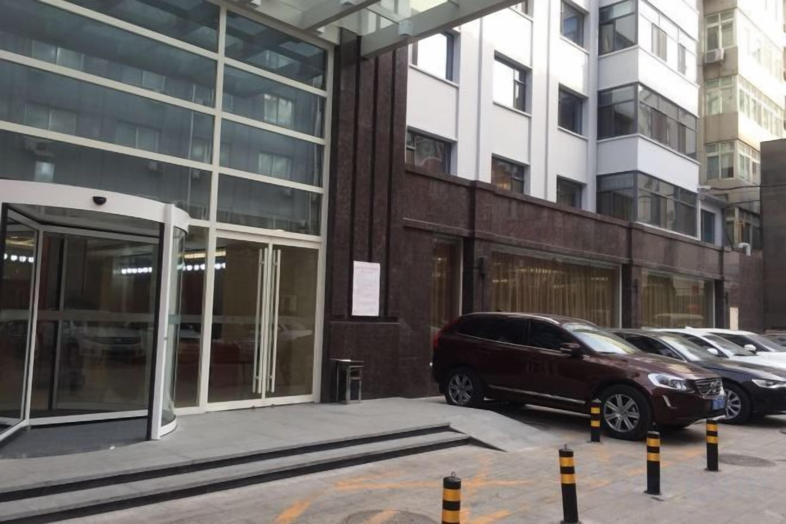 Un bâtiment moderne avec une entrée en verre, un parking avec des voitures et un hydrant d’incendie.