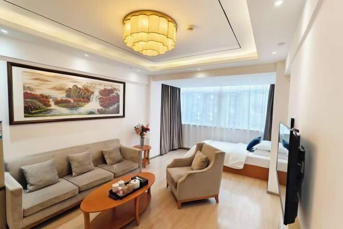 Una camera d'albergo con divano, poltrona, tavolino, letto, televisore e un quadro appeso al muro.
