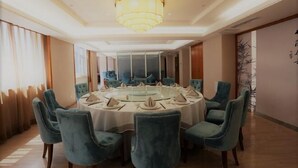 A dining area with a round table, blue upholstered chairs, and a chandelier. - Xuesong Hostel (Beijing)