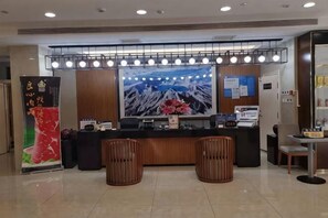 A hotel reception area with a large TV screen, a reception desk, two wooden chairs, and a bulletin board. - Xuesong Hostel (Beijing)