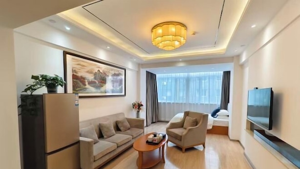 A modern living room with a sofa, armchair, coffee table, TV, and artwork on the wall. - Xuesong Hostel (Beijing)