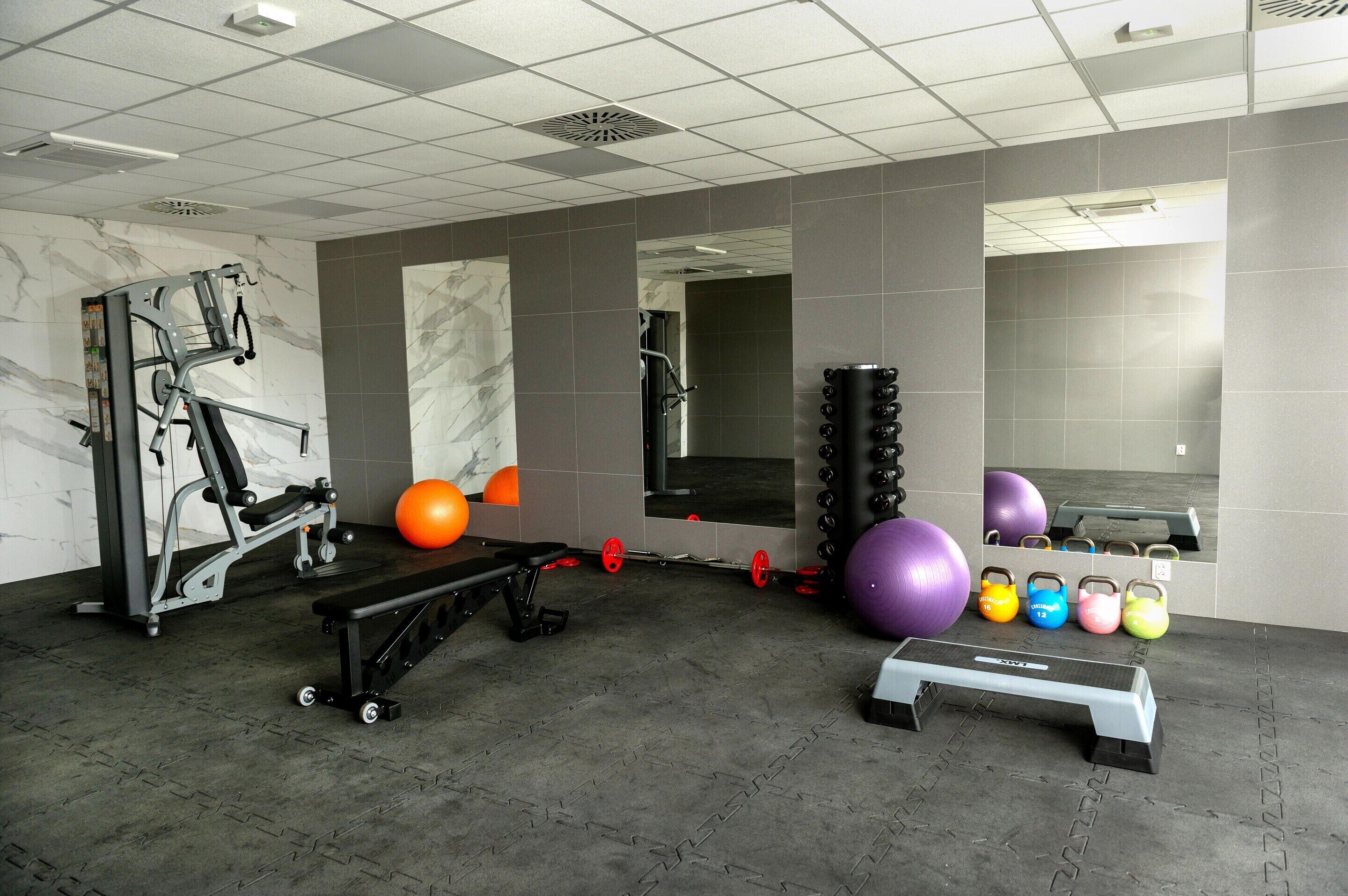 Une salle de sport équipée de matériel d’exercice, d’un banc et de différents ballons d’exercice.