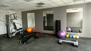 Une salle de sport équipée de matériel d’exercice, d’un banc et de différents ballons d’exercice.