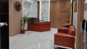 A reception area with a marble floor, a reception desk, a clock, a potted plant, and a red seating area. - Royal Rooms and Banquet (Lucknow)