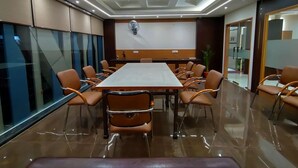 A conference room with a long table, chairs, a whiteboard, and a ceiling with recessed lighting.