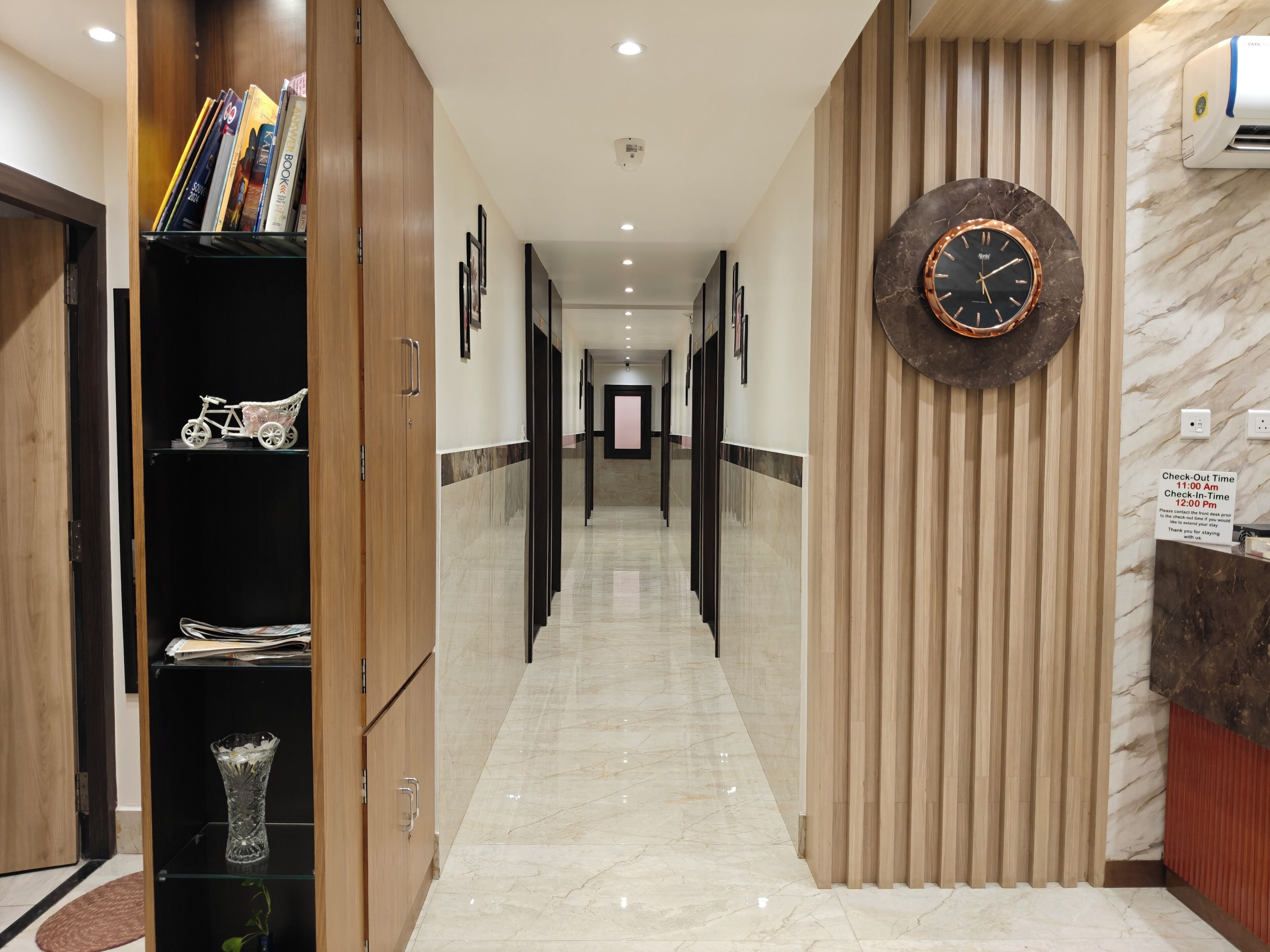 Pasillo de hotel con un cartel de hora de salida, un reloj y una recepción.