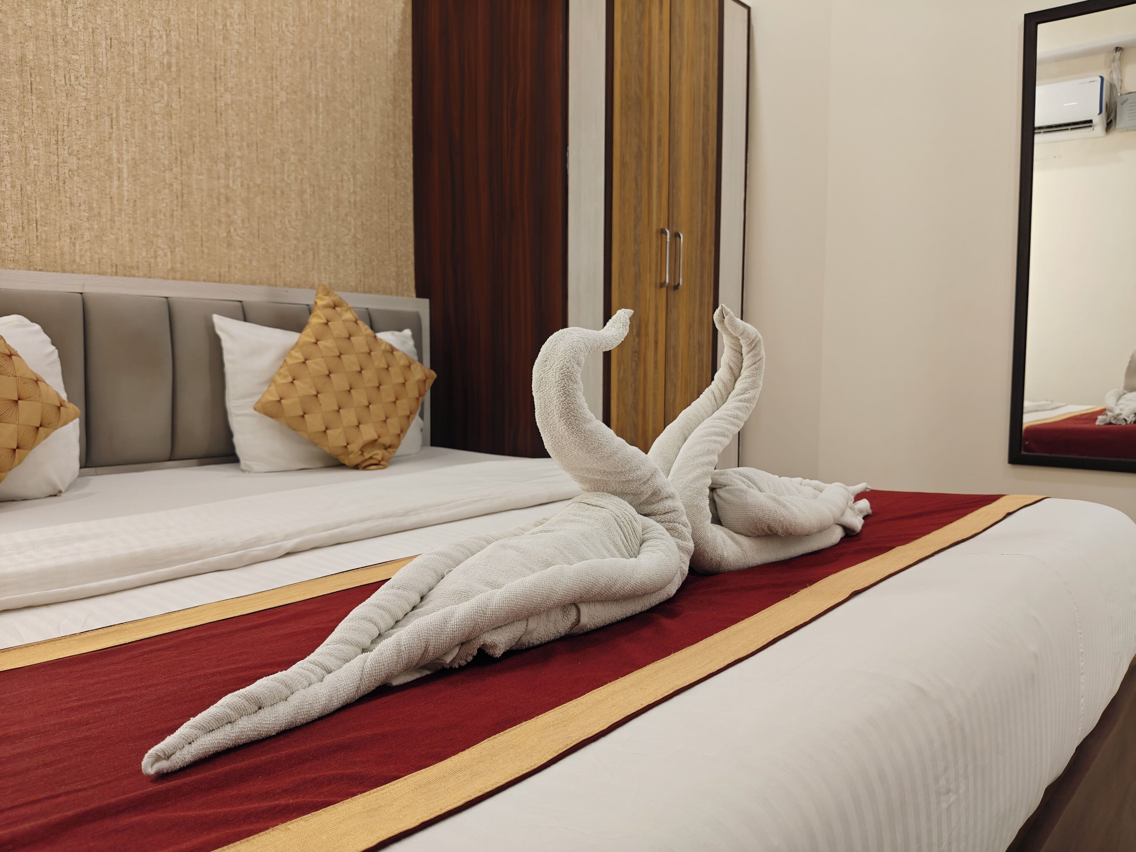 Habitación de hotel con una cama, una colcha a rayas rojas y doradas, y un espejo grande en la pared.