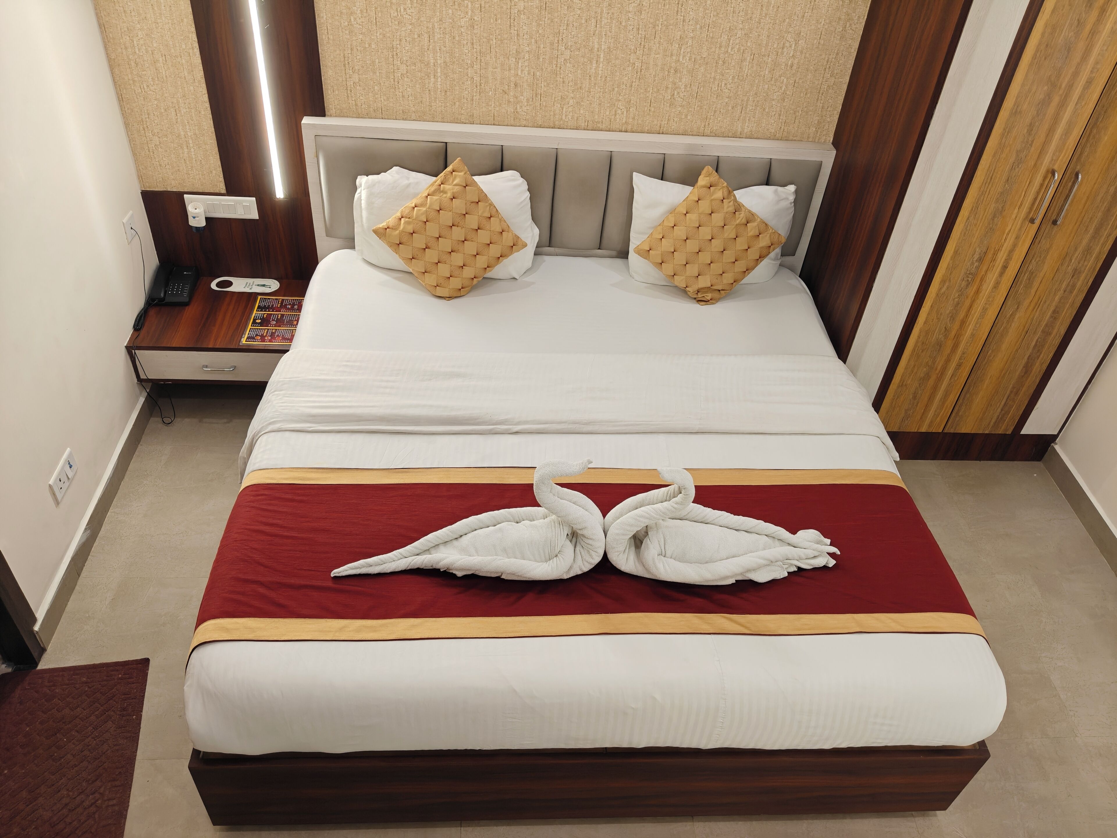 A hotel room with a bed, two pillows, a bedside table with a phone, and a red and white striped bedspread.