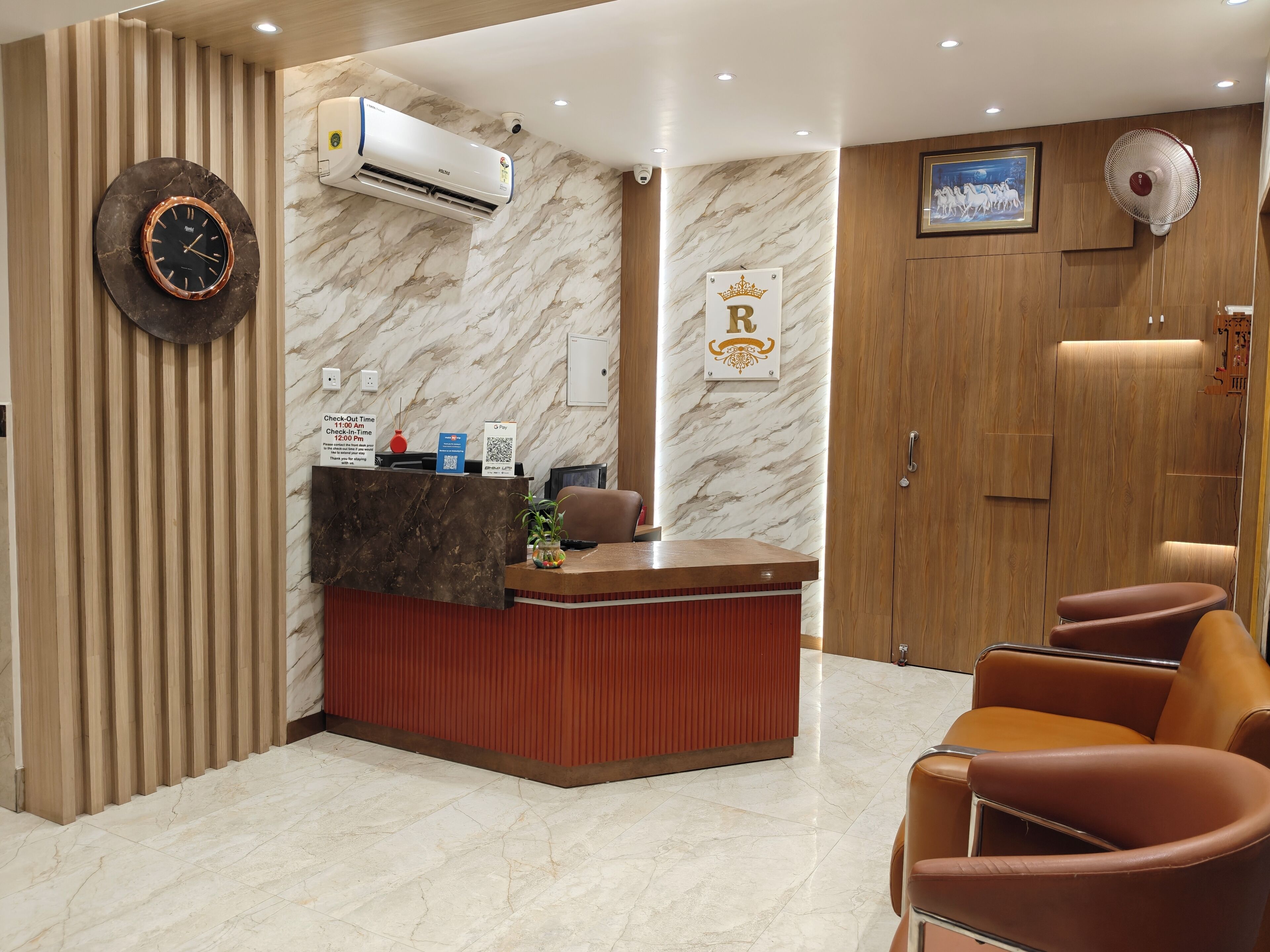 A hotel reception area with a marble wall, a reception desk, a clock, and a sign indicating check-in time.