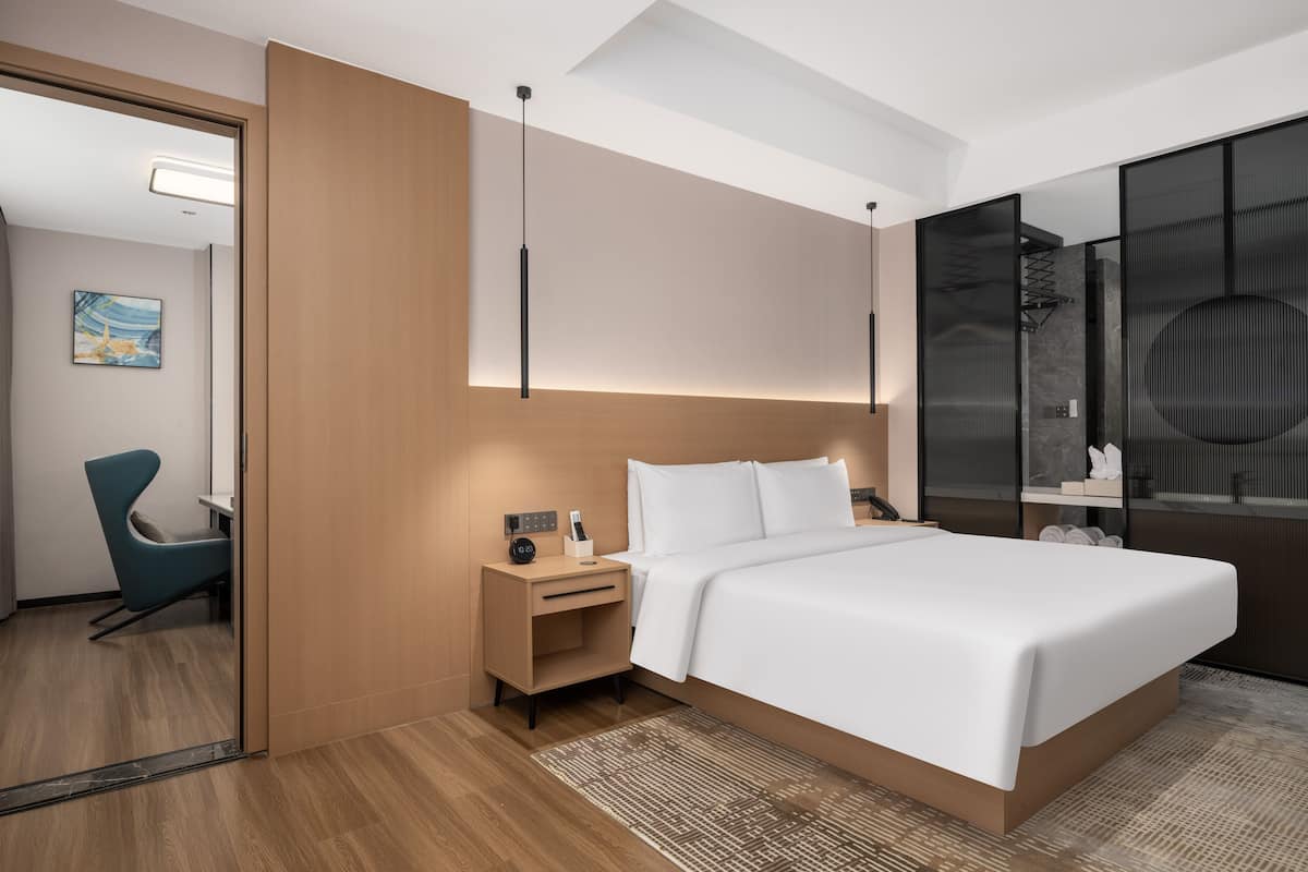 Ett modernt hotellrum med en stor säng, ett sängbord, en stol och en stor spegel.