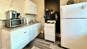 A compact kitchen with white cabinets, a microwave, a stove, and a refrigerator.