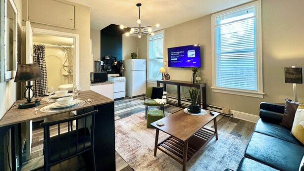 A modern apartment with a kitchen, dining area, and living room. It includes a TV, a dining table with chairs, a sofa, and a small coffee table.