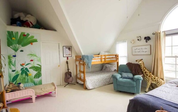 Ein gemütliches Schlafzimmer mit Etagenbett, Gitarre, Giraffe Stofftier und blauem Sessel.