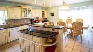 A kitchen with white cabinets, a black countertop, and a dining area with wooden chairs. - Panoramic Picturesque Home in Blue Ridge Mtns (Max Meadows)